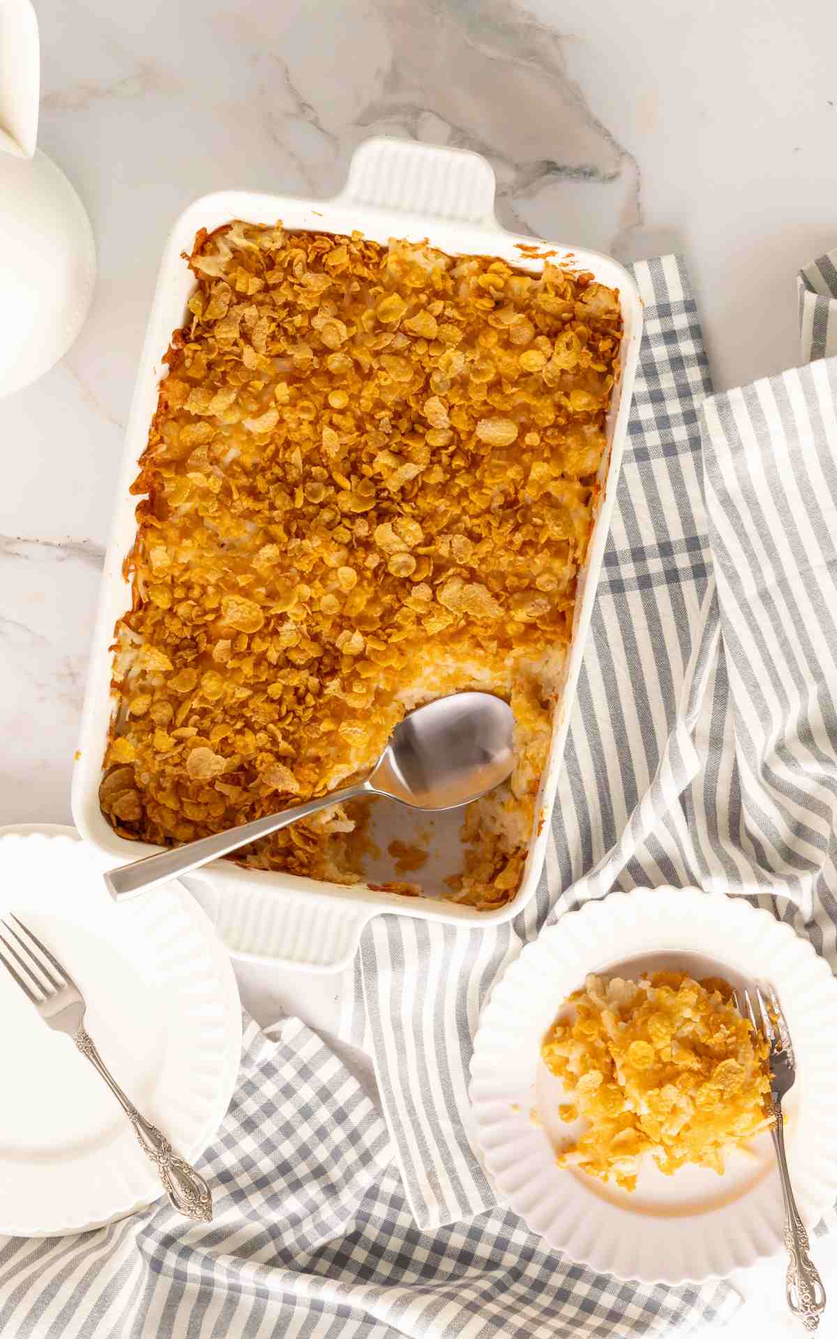 Cheesy hashbrown casserole in a baking dish with a plate and fork.