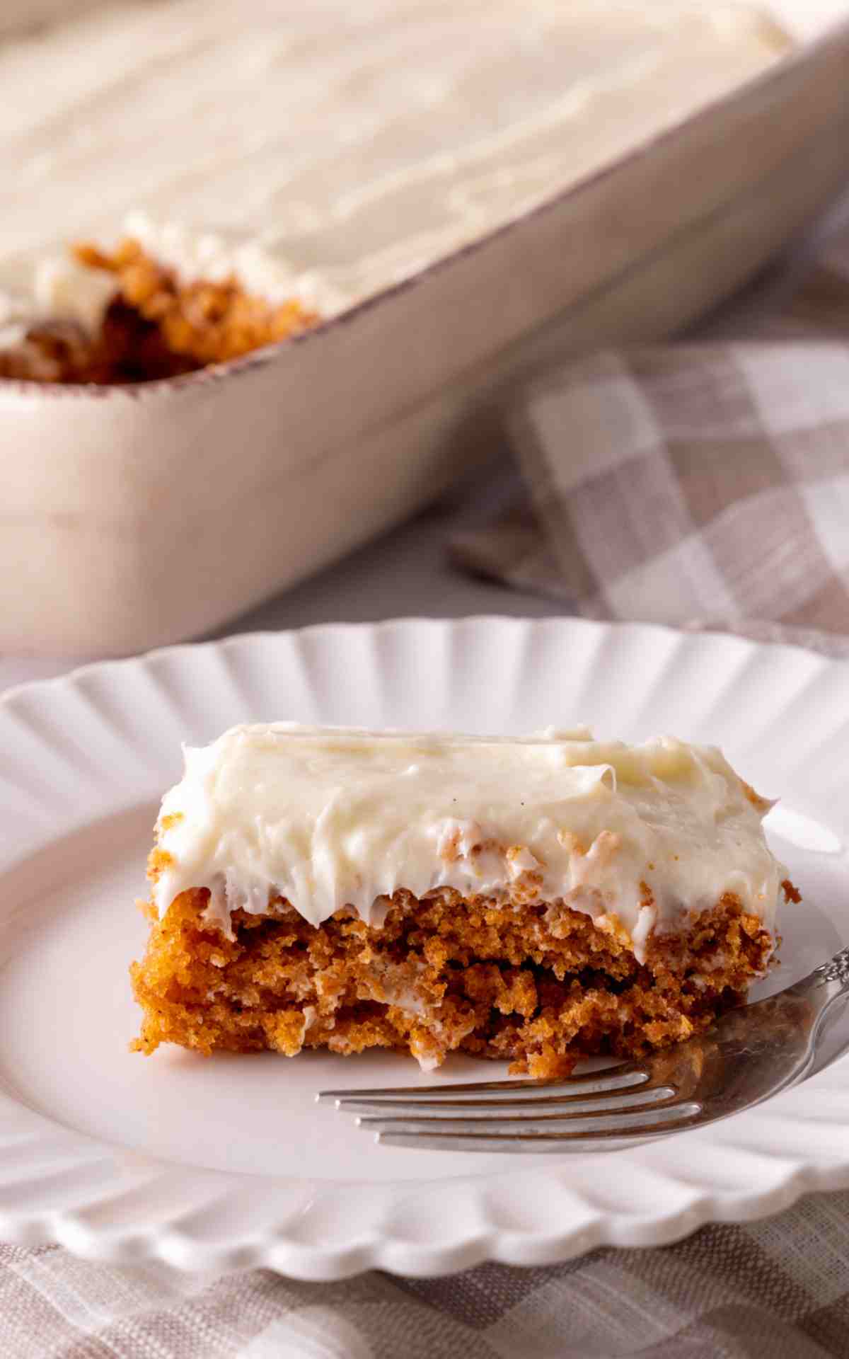 A slice of tomato soup cake on a scalloped plate that has homemade cream cheese frosting.