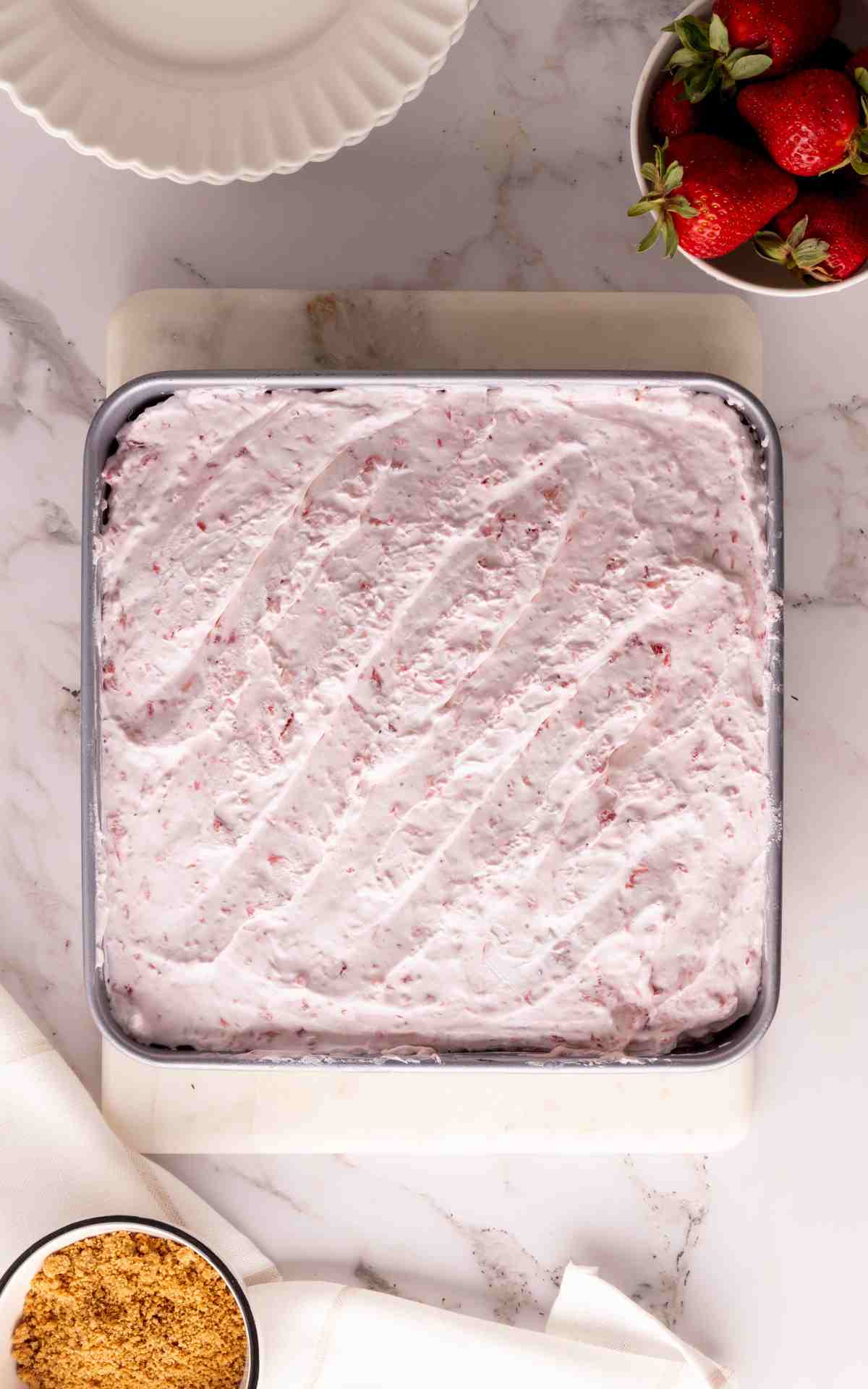 Cool Whip spread over top of cheesecake filling in a baking pan.