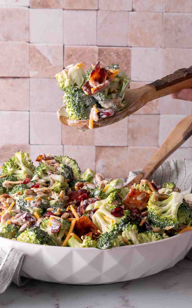 A wooden serving spoon with broccoli salad with cheese bacon and dressing.