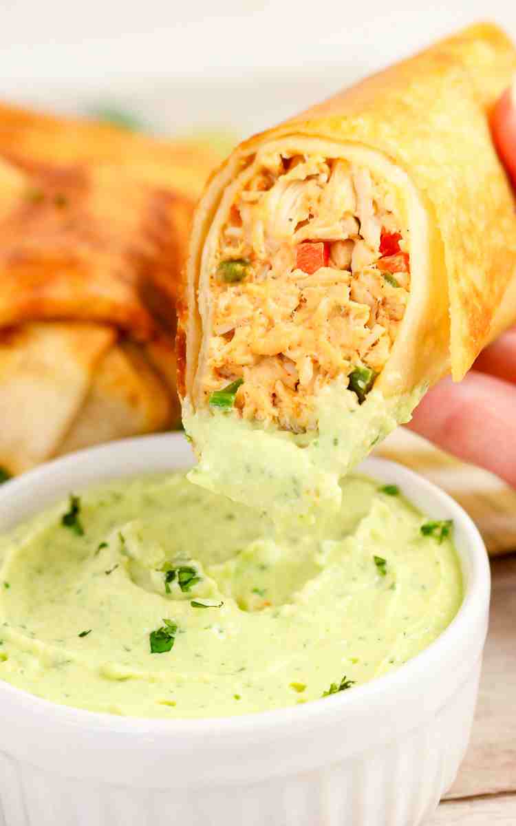 Firecracker chicken wrap being dipped into a bowl of avocado lime dip.