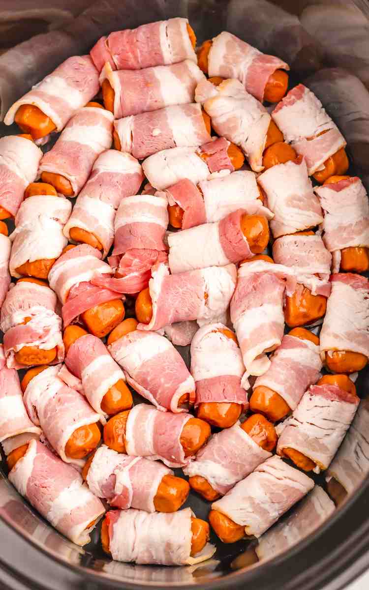 Uncooked little smokies wrapped in bacon in slow cooker.